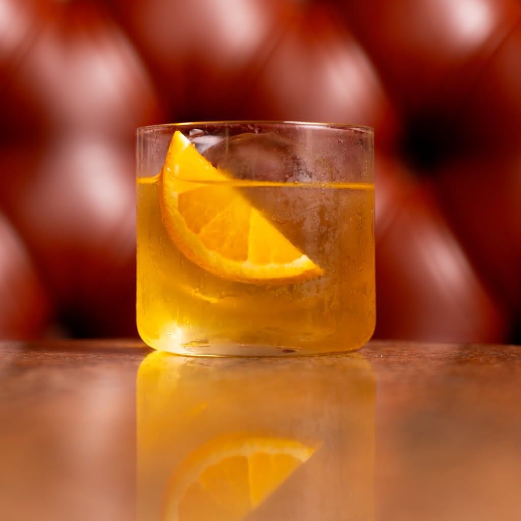 A lowball glass filled with a golden amber cocktail and a large orange wedge