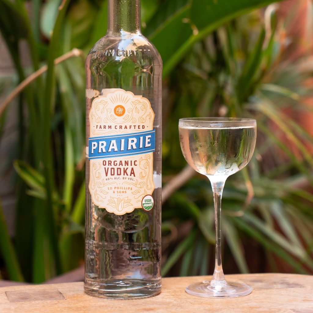 A bottle of Prairie Organic Vodka beside a clear, chilled cocktail in a delicate coupe glass