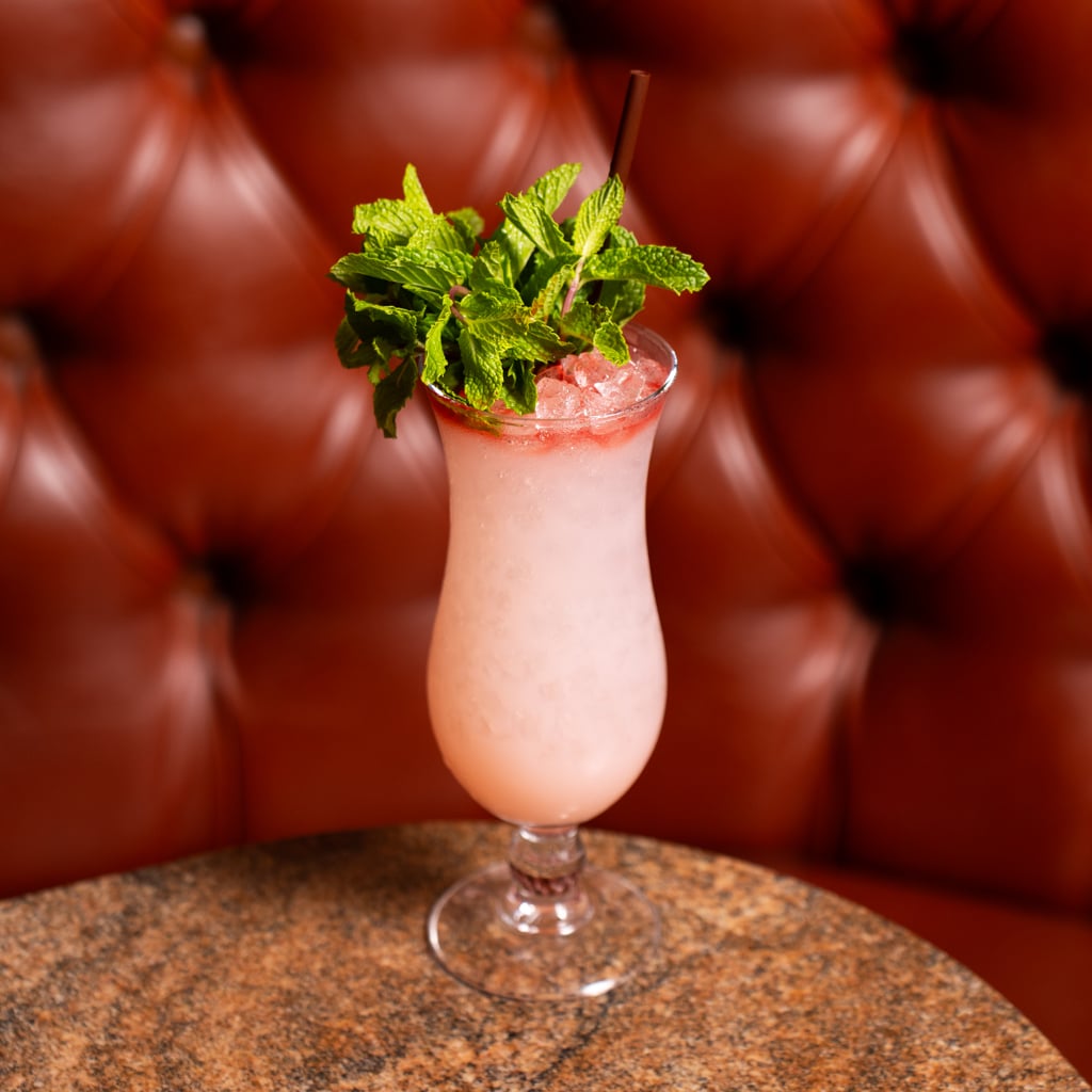 A frosty pale pink swizzle in a hurricane glass topped with crushed ice and a large bouquet of fresh mint